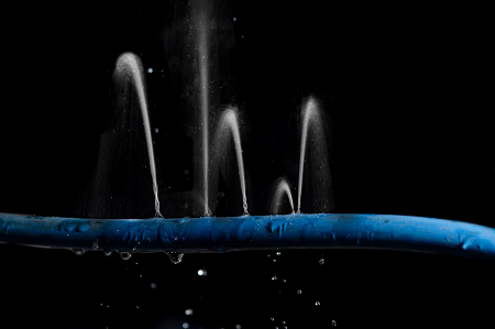 Aus einem Wasserschlauch schießen Fontänen durch Löcher im Schlacuhmantel